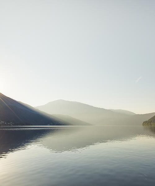 Der Millstätter See zwischen Berge und Hügel. Im Hintergrund geht die Sonne auf.