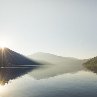 Der Millstätter See zwischen Berge und Hügel. Im Hintergrund geht die Sonne auf.