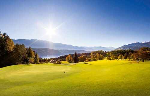A golf course in the bright sunshine with Lake Millstatt in the background